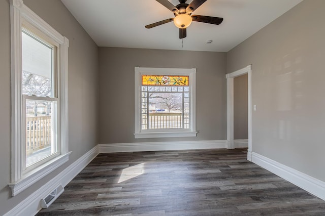 empty room with a ceiling fan, visible vents, dark wood finished floors, and baseboards