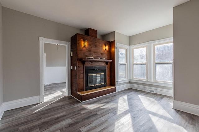 unfurnished living room with dark wood-style floors, a large fireplace, visible vents, and baseboards