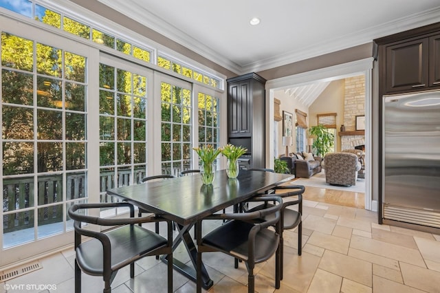 dining space with stone tile floors, visible vents, vaulted ceiling, crown molding, and a fireplace