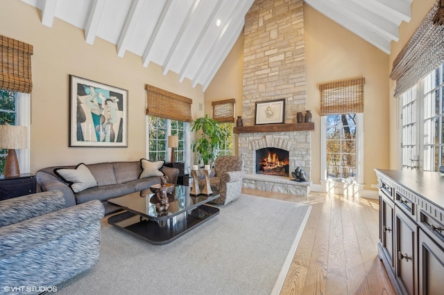 living area with high vaulted ceiling, light wood-type flooring, beam ceiling, and a stone fireplace