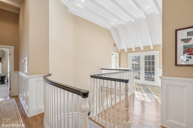 hall featuring light wood-style flooring, an upstairs landing, french doors, wainscoting, and beamed ceiling