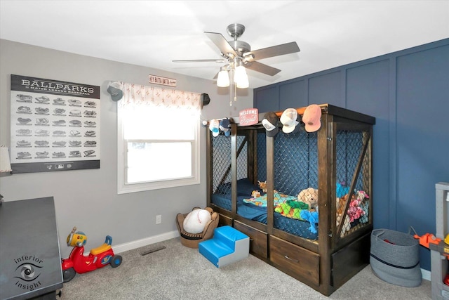 carpeted bedroom featuring a ceiling fan, visible vents, a decorative wall, and baseboards