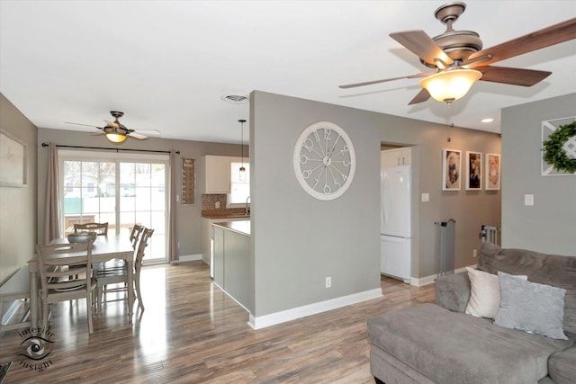 living room with a ceiling fan, baseboards, visible vents, and light wood finished floors