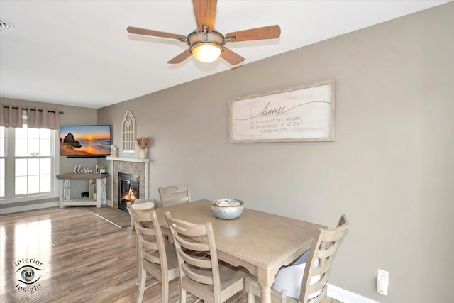 dining area with a ceiling fan, a glass covered fireplace, baseboards, and wood finished floors