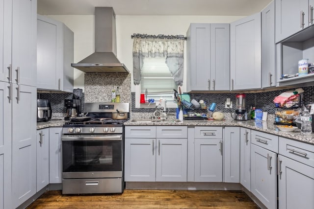 kitchen with light stone counters, stainless steel range with gas cooktop, dark wood-style floors, decorative backsplash, and wall chimney range hood
