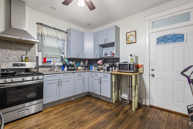 kitchen featuring light stone counters, appliances with stainless steel finishes, wall chimney range hood, dark wood-style floors, and open shelves