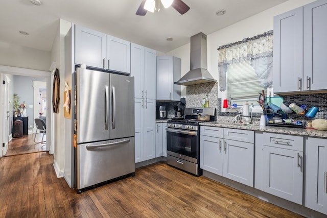 kitchen with decorative backsplash, dark wood finished floors, wall chimney exhaust hood, light stone counters, and stainless steel appliances