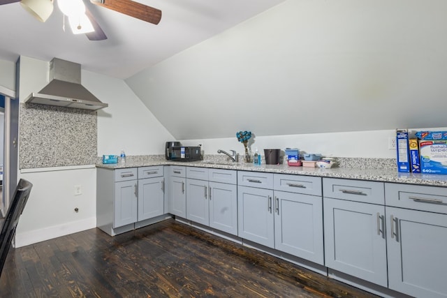 kitchen with wall chimney exhaust hood, vaulted ceiling, light stone counters, and dark wood finished floors