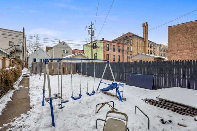 snow covered playground featuring a playground, fence, and a residential view