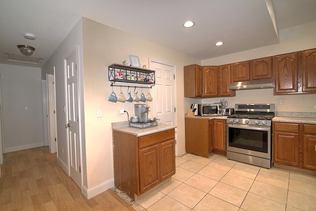 kitchen with stainless steel gas stove, under cabinet range hood, brown cabinetry, and light countertops