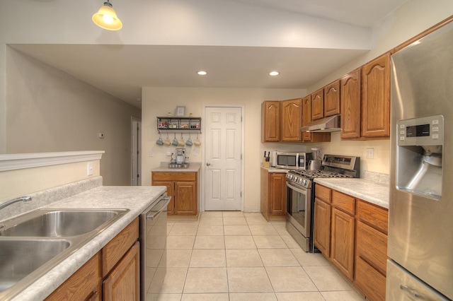 kitchen featuring appliances with stainless steel finishes, brown cabinets, under cabinet range hood, a sink, and recessed lighting