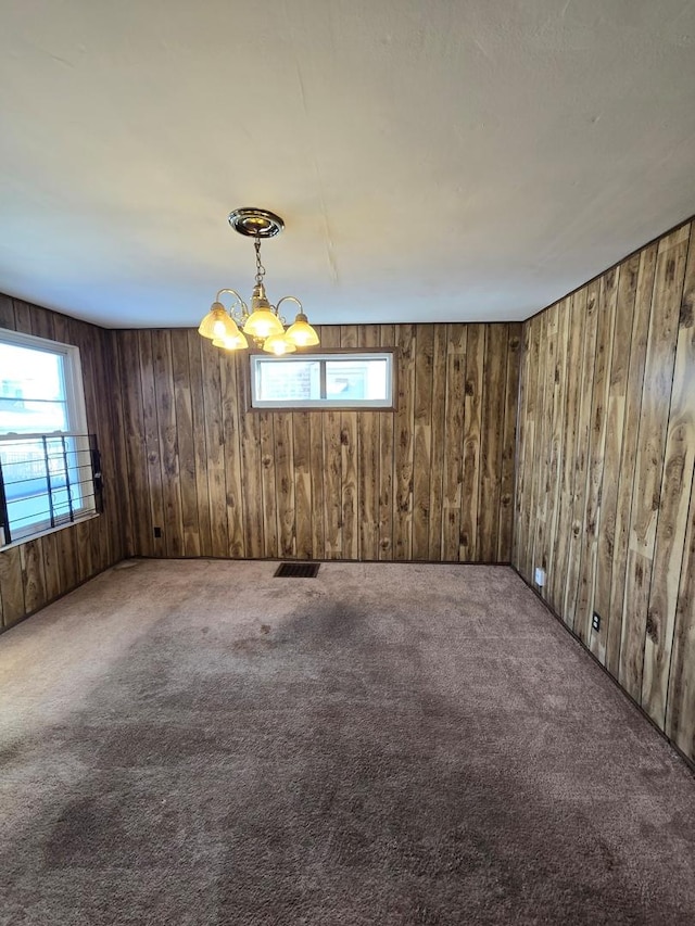 unfurnished room featuring an inviting chandelier, wooden walls, visible vents, and carpet flooring