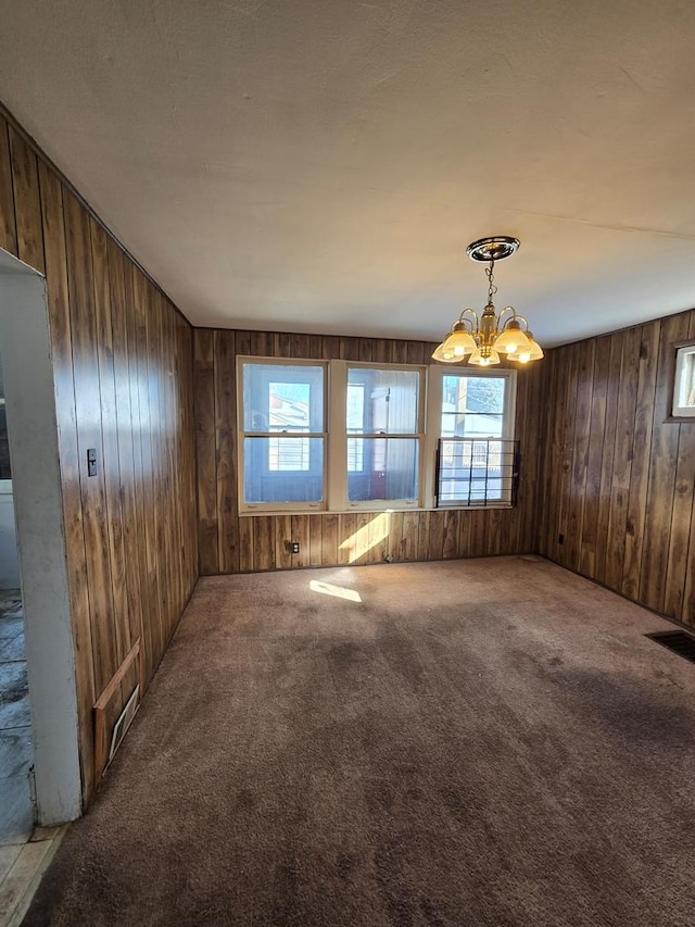 carpeted empty room featuring a chandelier, wood walls, and visible vents