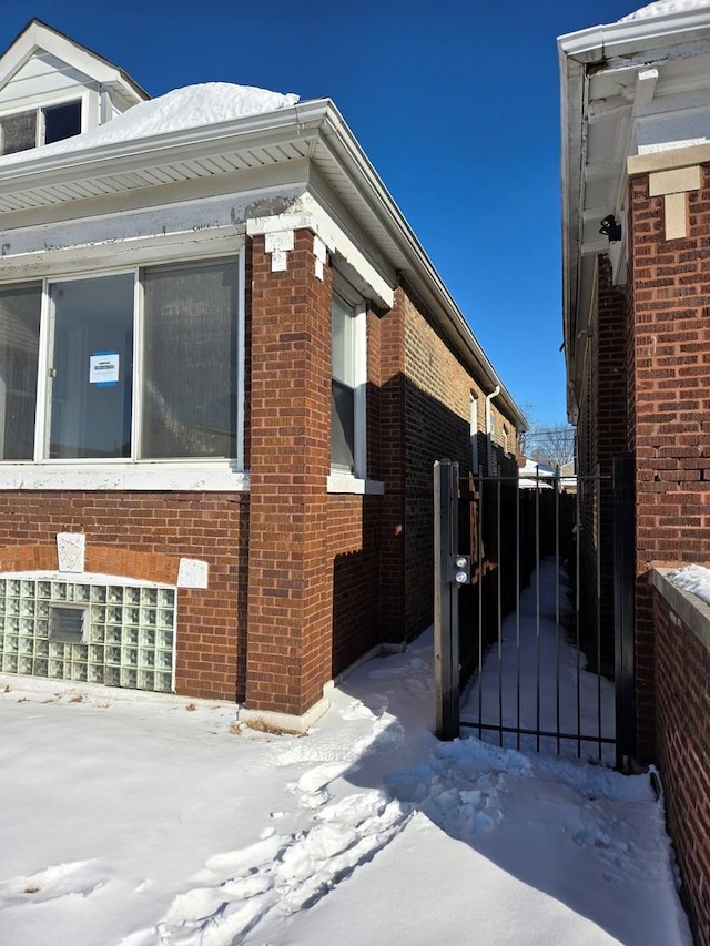 view of snowy exterior featuring brick siding and a gate