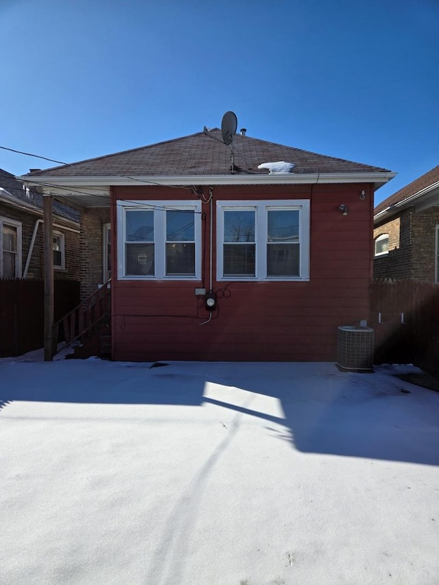 snow covered rear of property featuring central AC unit