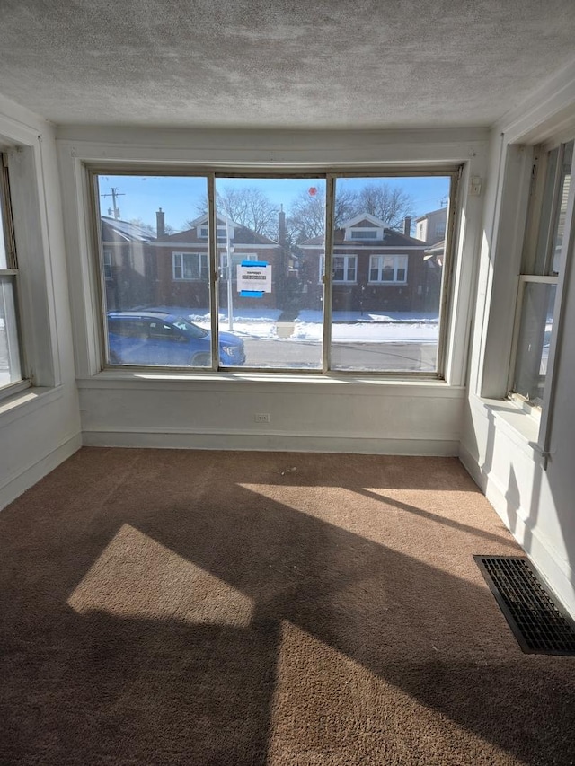 carpeted empty room with a textured ceiling, visible vents, and baseboards