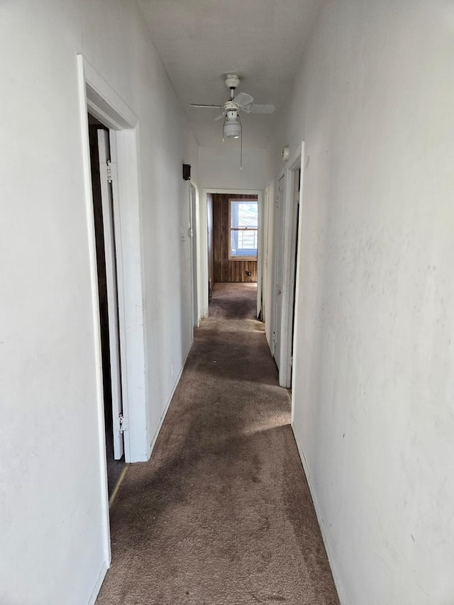 hall featuring dark carpet and baseboards