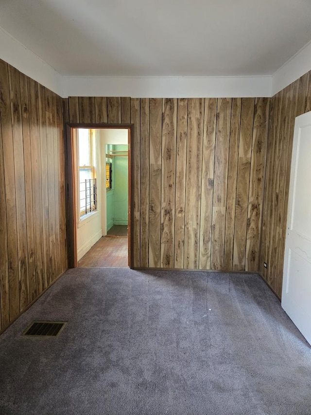 carpeted spare room featuring wood walls and visible vents