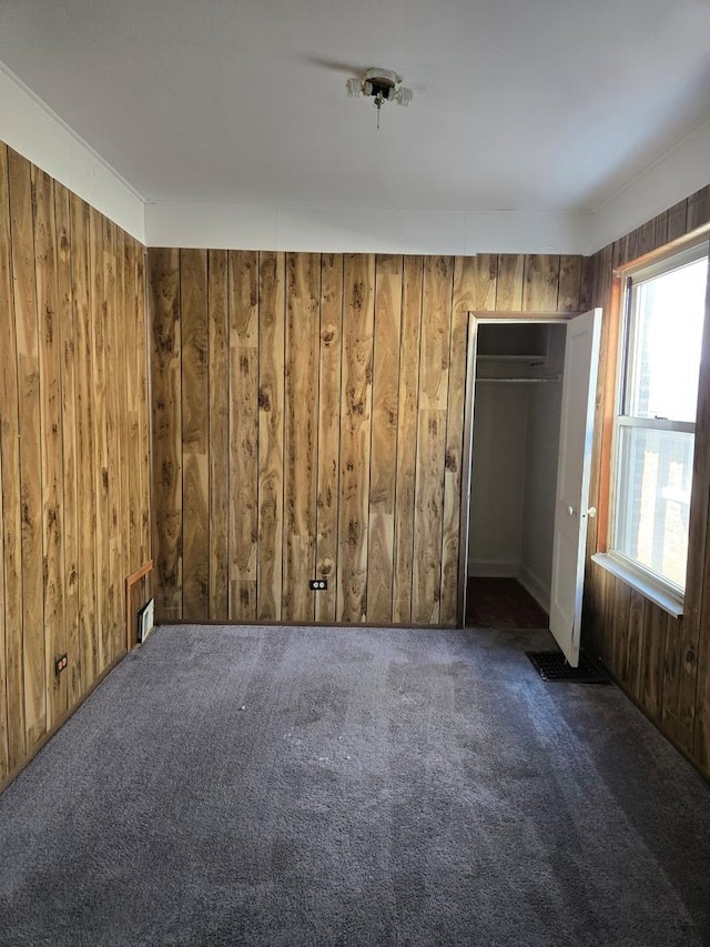 spare room featuring dark colored carpet and wooden walls