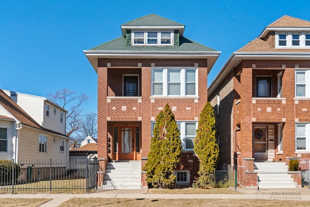 view of front of home with a fenced front yard, a shingled roof, and brick siding