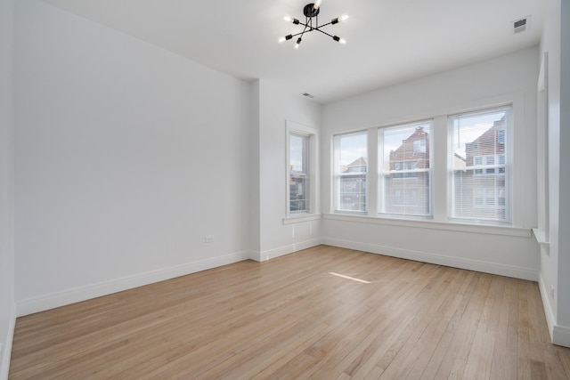 spare room featuring a chandelier, light wood-type flooring, visible vents, and baseboards