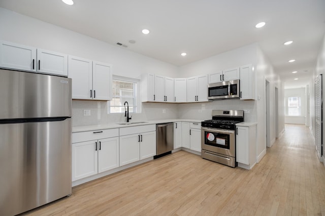 kitchen featuring light wood finished floors, tasteful backsplash, stainless steel appliances, light countertops, and a sink