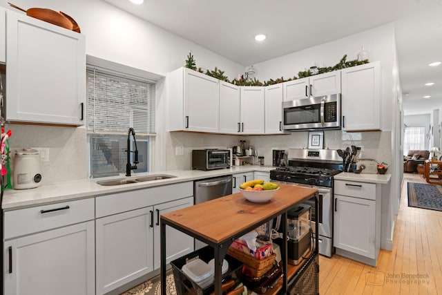 kitchen with light wood-style flooring, a sink, light countertops, appliances with stainless steel finishes, and decorative backsplash