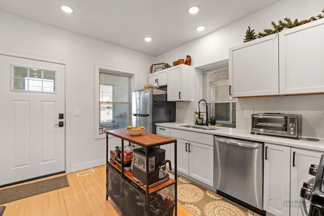 kitchen with stainless steel appliances, light countertops, a sink, and light wood-style flooring