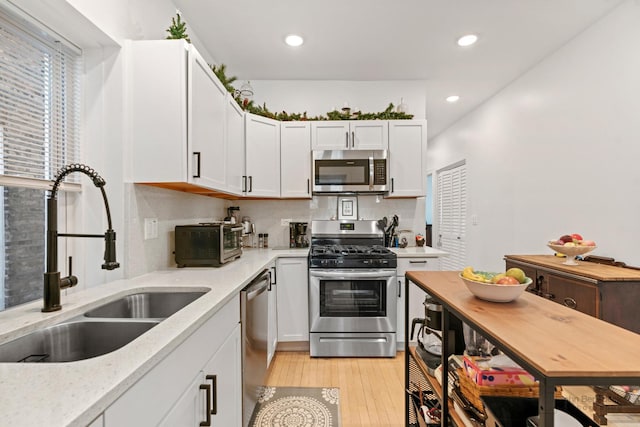 kitchen featuring backsplash, light wood-style flooring, appliances with stainless steel finishes, white cabinetry, and a sink