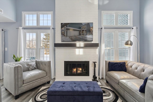 living area with light wood finished floors, a brick fireplace, and visible vents