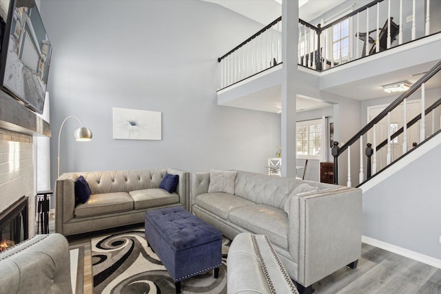 living area with wood finished floors, a towering ceiling, baseboards, stairs, and a glass covered fireplace