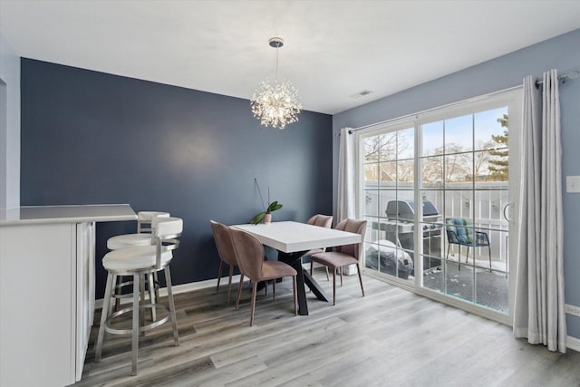 dining space with light wood finished floors, baseboards, visible vents, and a notable chandelier