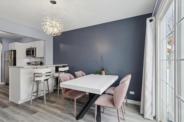 dining area featuring light wood-style floors, baseboards, and a notable chandelier