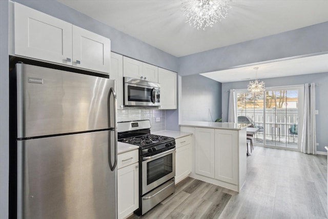 kitchen with appliances with stainless steel finishes, a peninsula, an inviting chandelier, light countertops, and white cabinetry