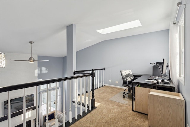 home office featuring vaulted ceiling with skylight, baseboards, a ceiling fan, and light colored carpet