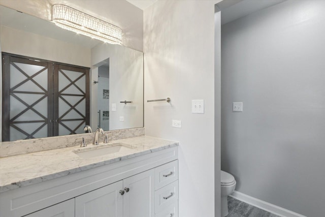 bathroom with toilet, vanity, baseboards, and wood finished floors