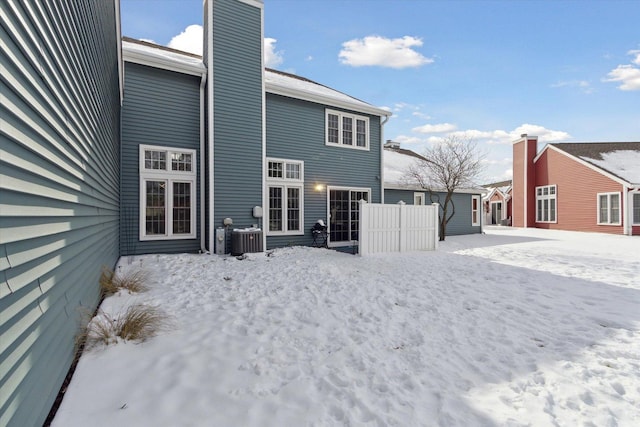 snow covered house featuring a chimney, central AC unit, and fence