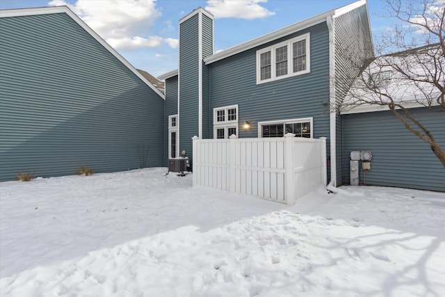 snow covered house with a chimney, fence, and cooling unit