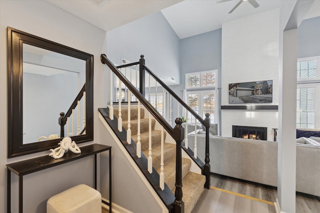 staircase featuring a large fireplace, a ceiling fan, and wood finished floors