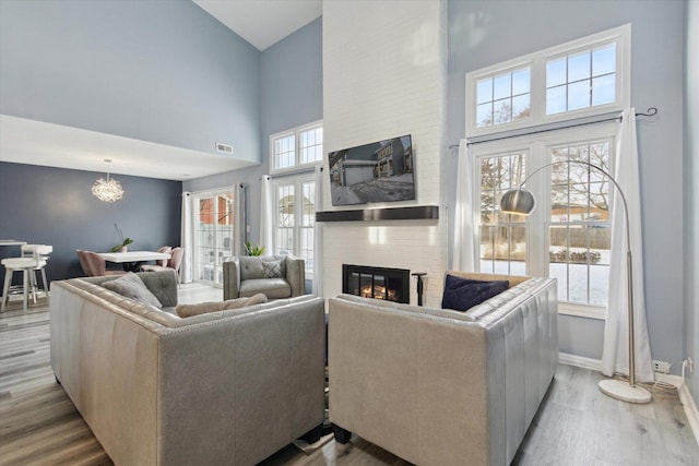 living area with a large fireplace, a high ceiling, visible vents, baseboards, and light wood-style floors