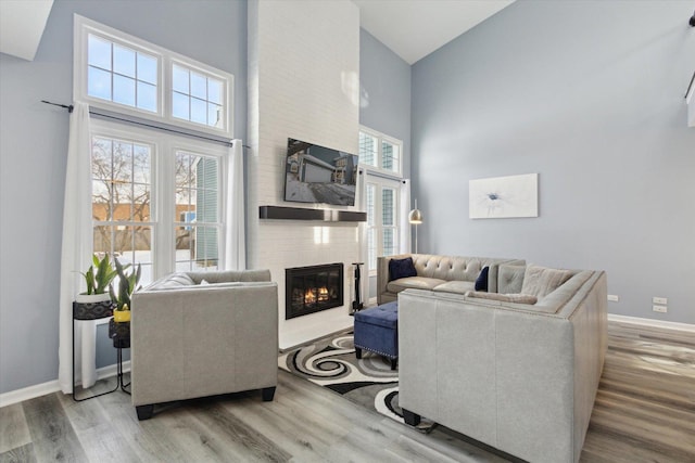 living area with a large fireplace, a high ceiling, baseboards, and wood finished floors