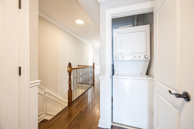 laundry area featuring a decorative wall, laundry area, stacked washer / dryer, dark wood finished floors, and crown molding