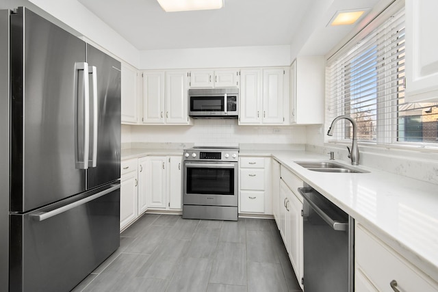 kitchen with light countertops, decorative backsplash, appliances with stainless steel finishes, white cabinets, and a sink