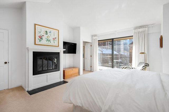 bedroom with access to outside, a glass covered fireplace, vaulted ceiling, and carpet