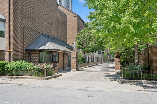 view of front of house featuring a standing seam roof, a gate, metal roof, and brick siding