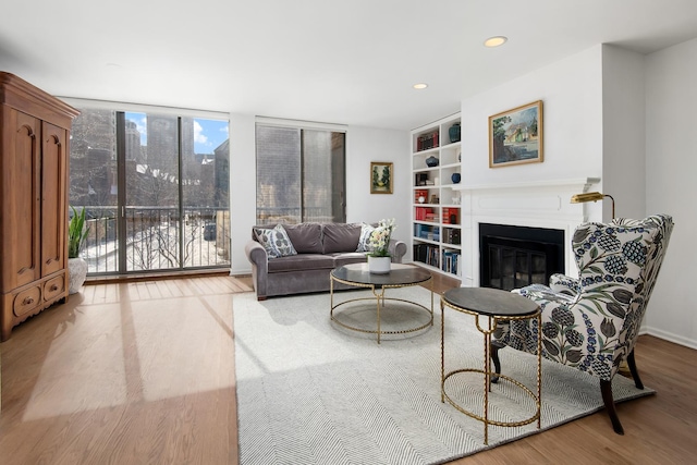 living area featuring a glass covered fireplace, wood finished floors, expansive windows, built in shelves, and recessed lighting