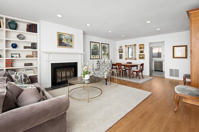 living area with a fireplace with flush hearth, visible vents, wood finished floors, and recessed lighting