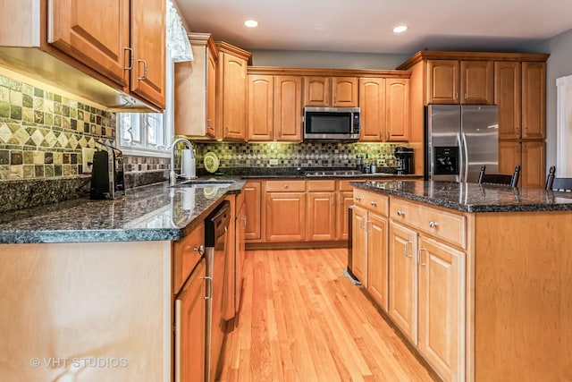 kitchen with dark stone counters, decorative backsplash, light wood-style flooring, stainless steel appliances, and a sink