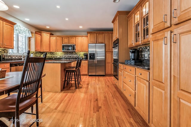 kitchen with light wood finished floors, a kitchen island, glass insert cabinets, a kitchen bar, and stainless steel appliances