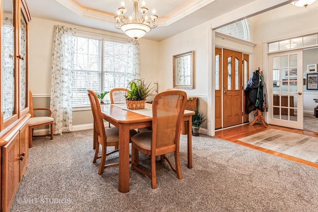 carpeted dining room with an inviting chandelier, a tray ceiling, crown molding, and baseboards